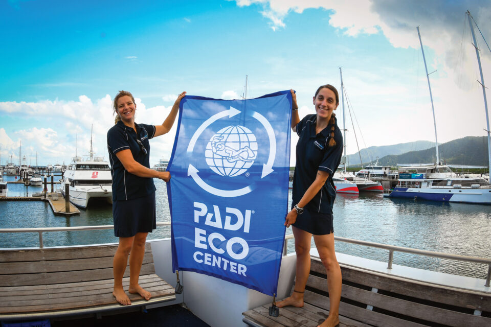 Two crew members standing on the boat holding a Padi Eco Centre banner.